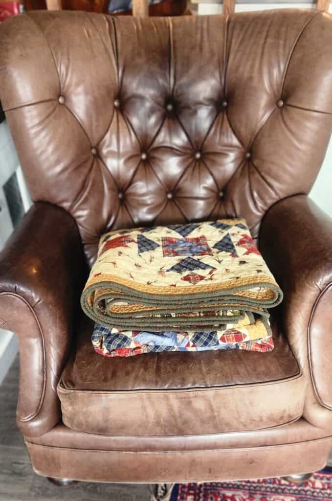 Folded quilt in an brown leather arm chair.