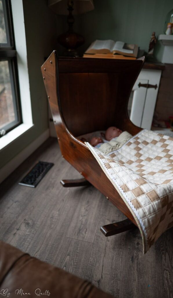 Old fashioned wooden cradle with an Irish Chain quilt draped over it.