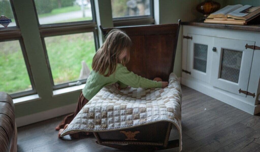 Girl tucking in her dolls with an Irish Chain baby quilt